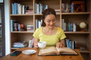 ung kvinna läsning bok och dryck varm kaffe i bibliotek på Hem, leende, skrattande, njuter bokmaskar hobby, Hem fritid tid foto