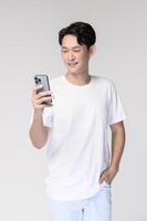 porträtt av ung leende asiatisk man använder sig av smartphone över vit bakgrund foto