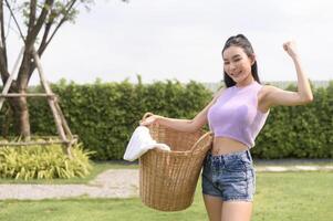 ung asiatisk kvinna innehav tvätt korg i bakgård utomhus- foto