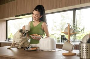 asiatisk kvinna framställning kaffe och rostat bröd bröd för frukost njut av med hund på de kök tabell i de morgon- foto