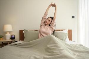 ung asiatisk kvinna stretching i säng efter vakna upp i de morgon- foto