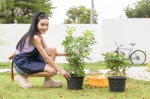 ung asiatisk kvinna plantering träd i de trädgård utomhus på Hem. foto