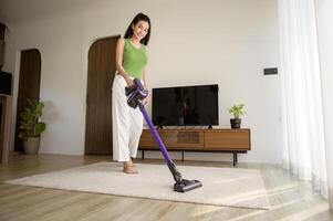 ung Lycklig kvinna använder sig av en Vakuum rengöringsmedel de golv i levande rum foto