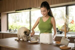 asiatisk kvinna framställning kaffe och rostat bröd bröd för frukost njut av med hund på de kök tabell i de morgon- foto