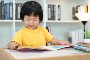 Lycklig asiatisk barn koppla av läsa bok på Hem. dotter och läsning en berättelse. lära sig utveckling, barnomsorg, skrattande, utbildning, berättande, öva, tänka, minska missbruk mobil telefon foto