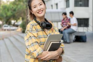 skön studerande asiatisk kvinna med ryggsäck och böcker utomhus. leende flicka Lycklig bärande en massa av bok i högskola campus. porträtt kvinna på internationell Asien universitet. utbildning, studie, skola foto
