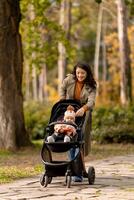 ung kvinna med söt bebis flicka i bebis sittvagn på de höst parkera foto