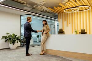 värma handslag mellan kollegor i modern kontor lobby under omgivande belysning foto
