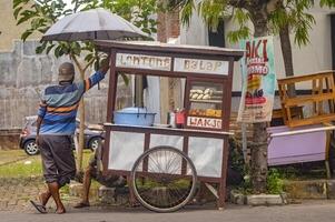 en gata säljare skjuta på vagn försäljning gata mat, nämligen långa balap, Indonesien, 16 januari 2024. foto