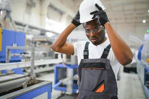 porträtt av afrikansk amerikan manlig ingenjör i enhetlig och stående i industriell fabrik foto