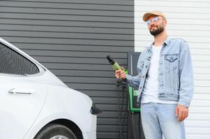 man innehav kraft laddning kabel- för elektrisk bil i utomhus- bil parkera. och han s gående till ansluta de bil till de laddning station i de parkering massa nära de handla Centrum. foto