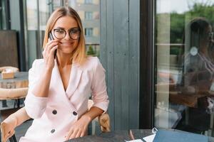 leende affärskvinna klädd i formell ha på sig har trevlig konversation på mobil telefon med vän, Lycklig attraktiv kvinna tala på cell telefon medan vilar i kontor interiör efter arbete foto