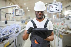 porträtt av industriell ingenjör. leende fabrik arbetstagare med hård hatt stående i fabrik produktion linje foto