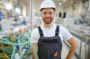 leende och Lycklig anställd. industriell arbetstagare inomhus i fabrik. ung tekniker med hård hatt foto