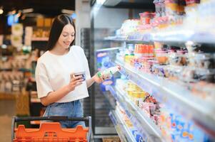 ung nöjd roligt kvinna i tillfällig kläder handla på supermarket Lagra med matvaror vagn foto
