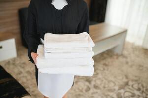 hembiträde innehav färsk handdukar med blommor i hotell rum foto
