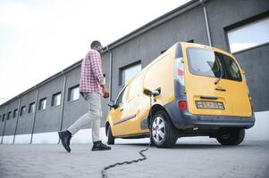 afrikansk amerikan man står Nästa till elektrisk leverans vans på elektrisk fordon laddning station foto
