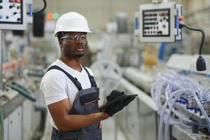 porträtt av afrikansk amerikan manlig ingenjör i enhetlig och stående i industriell fabrik foto