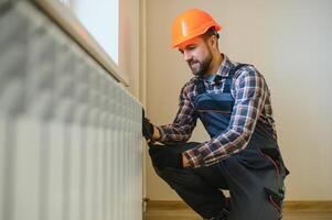 ung man rörmokare kontroll radiator medan montera uppvärmning systemet i lägenhet foto