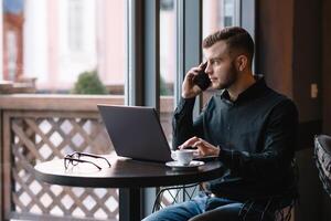 ung affärsman talande på mobil telefon medan arbetssätt på bärbar dator i Kafé. foto