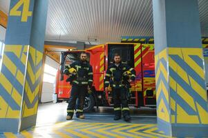 porträtt av två ung brandmän i enhetlig stående inuti de brand station foto