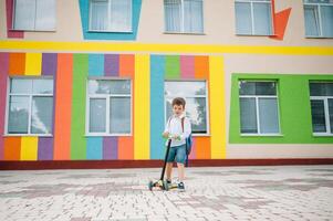 pojke går till skola på en skoter. barn tillbaka till skola skoter.barnskola ridning en skoter. tillbaka till skola. Lycklig barn. Lycklig barndom livsstil. studerande går till skola foto