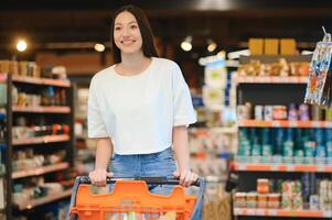 Lycklig ung kvinna ser på produkt på matvaror Lagra. leende kvinna handla i mataffär foto