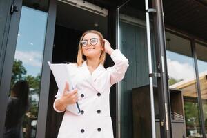 porträtt av en framgångsrik affärskvinna innehav en digital läsplatta vaddera och en mapp medan stolt stående nära kontor. foto