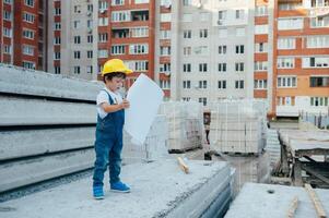 arkitekt i hjälm skrivning något nära ny byggnad. liten söt pojke på de byggnad som ett arkitekt foto