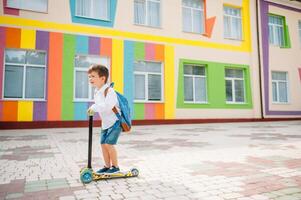 pojke går till skola på en skoter. barn tillbaka till skola skoter.barnskola ridning en skoter. tillbaka till skola. Lycklig barn. Lycklig barndom livsstil. studerande går till skola foto