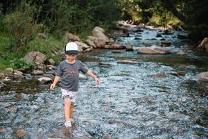 Lycklig pojke på en promenad nära de flod i de bergen foto