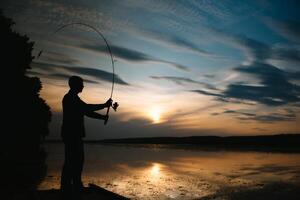 fiskare på solnedgång på de flod .skön sommar landskap med solnedgång på de flod. fiske. spinning på solnedgång. silhuett av en fiskare foto