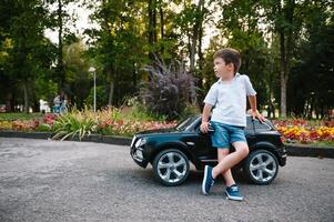 söt pojke i ridning en svart elektrisk bil i de parkera. rolig pojke rider på en leksak elektrisk bil. kopia Plats. foto