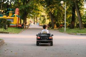 söt pojke i ridning en svart elektrisk bil i de parkera. rolig pojke rider på en leksak elektrisk bil. kopia Plats. foto