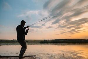 fiske. spinning på solnedgång. silhuett av en fiskare foto