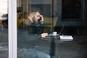 ung affärsman talande på mobil telefon medan arbetssätt på bärbar dator i Kafé. foto