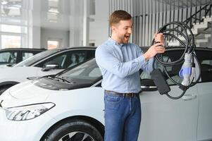 ung man, försäljning elektrisk bilar i de showroom. begrepp av uppköp miljövänlig bil för familj foto