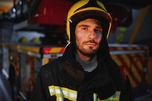 porträtt av en brandman i en skyddande kostym och en skyddande hjälm stående förbi en brand motor efter arbetssätt på en brand. närbild bild foto