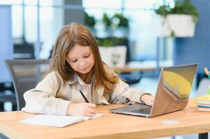 först dag på skola. söt och Lycklig liten flicka barn använder sig av bärbar dator dator, studerar genom uppkopplad e-learning systemet foto