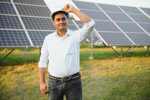 porträtt av ung indisk manlig ingenjör stående nära sol- paneler, med klar blå himmel bakgrund, förnybar och rena energi. skicklighet Indien, kopia Plats foto