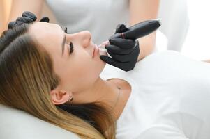 ung kvinna har permanent smink på mun i kosmetolog salong foto