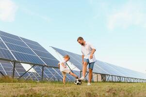 far och son ha roligt spelar fotboll nära de sol- paneler. de begrepp av grön energi foto