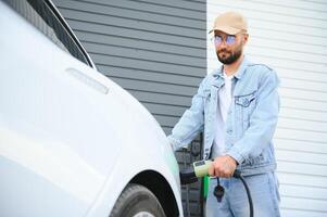 skön ung eleganta man är med elektrisk bil på dagtid laddning de fordon foto