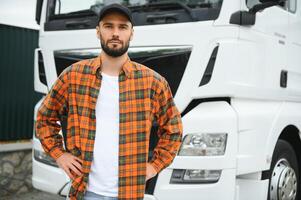 porträtt av ung skäggig trucker stående förbi hans lastbil fordon. transport service. lastbil förare jobb foto