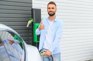 man innehav kraft laddning kabel- för elektrisk bil i utomhus- bil parkera. och han s gående till ansluta de bil till de laddning station i de parkering massa nära de handla Centrum. foto