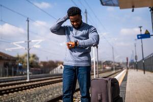 orolig man ser på hans klocka medan stående med resväska på en järnväg station. foto