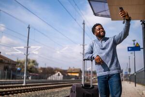Lycklig man med en resväska tar selfie på en järnväg station. foto