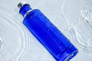 parfym mörk blå transparent flaska i vatten bakgrund foto