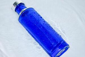 parfym mörk blå transparent flaska i vatten bakgrund foto