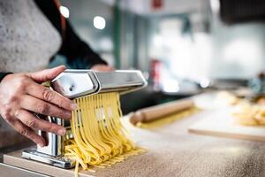 stänga upp av kvinna händer framställning färsk pasta använder sig av traditionell maskin - kök och mat begrepp foto